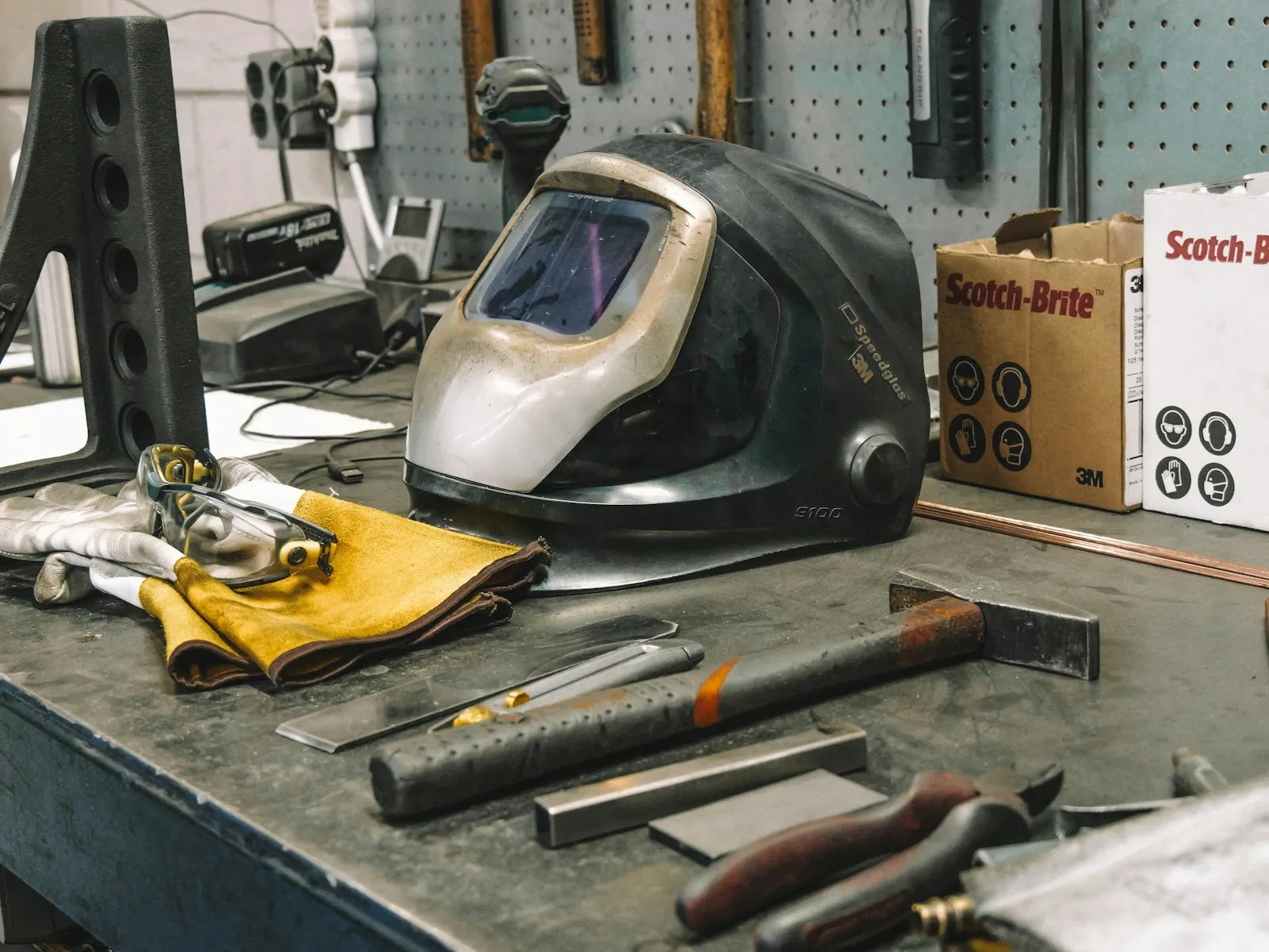 Welding helmet, gloves, and hand tools arranged on a workshop bench