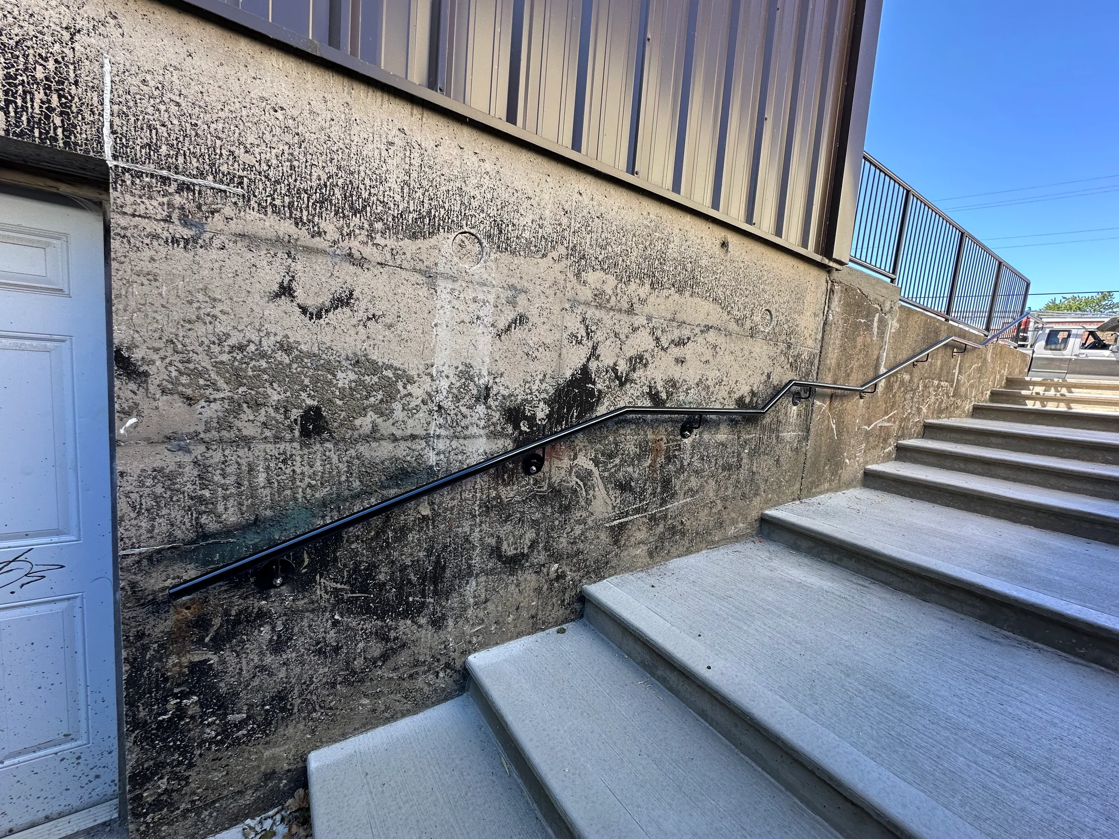 Wall-mounted handrail along concrete steps by BriteArc Fabricators