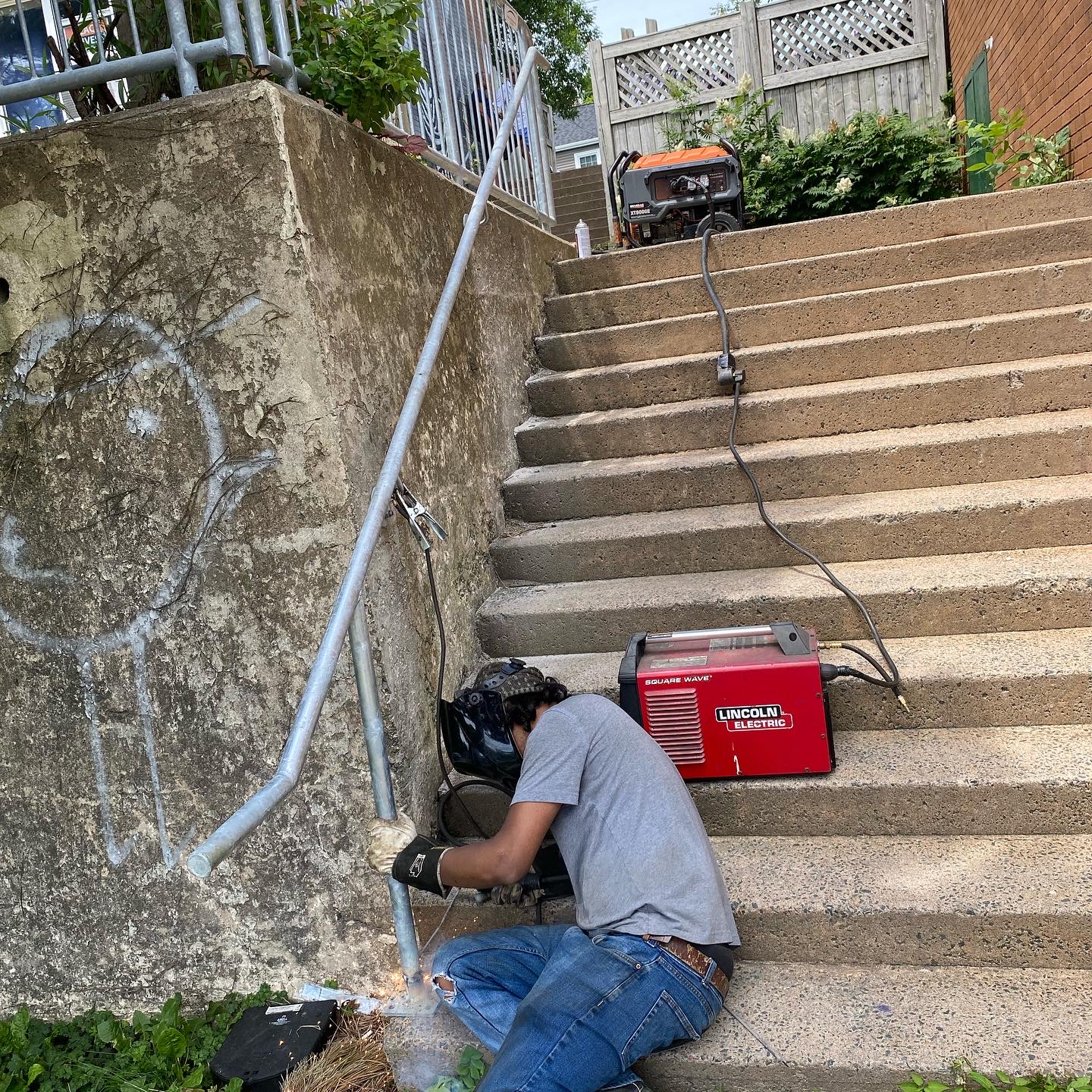 Welder completing field installation of a galvanized handrail at concrete stairs